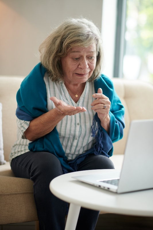 Elderly woman looking confused while using laptop computer