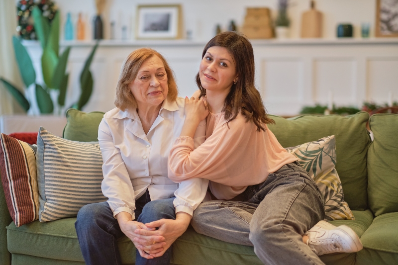 Grandmother and adult granddaughter sitting together on couch having conversation