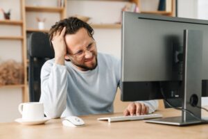 Man looking frustrated while working on computer with technology problems. digital overwhelm simplifying online life