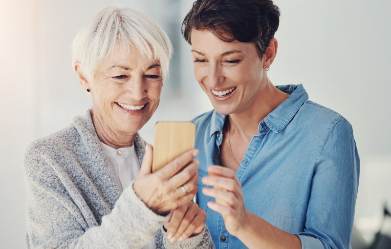 Elderly mother and adult daughter looking at smartphone together discussing digital accounts